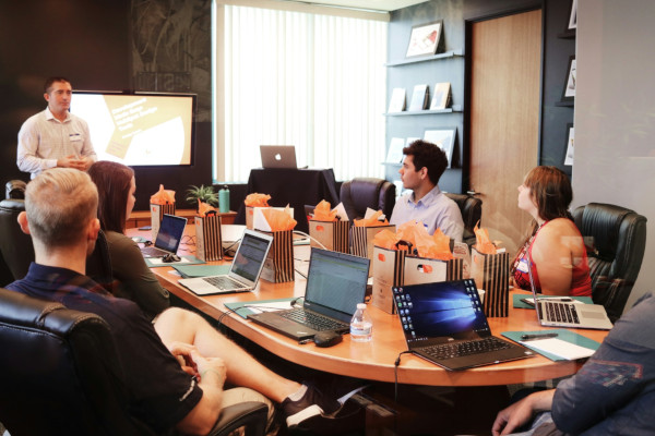 Business meeting with man standing in front of group of coworkers showing them charts on a screen